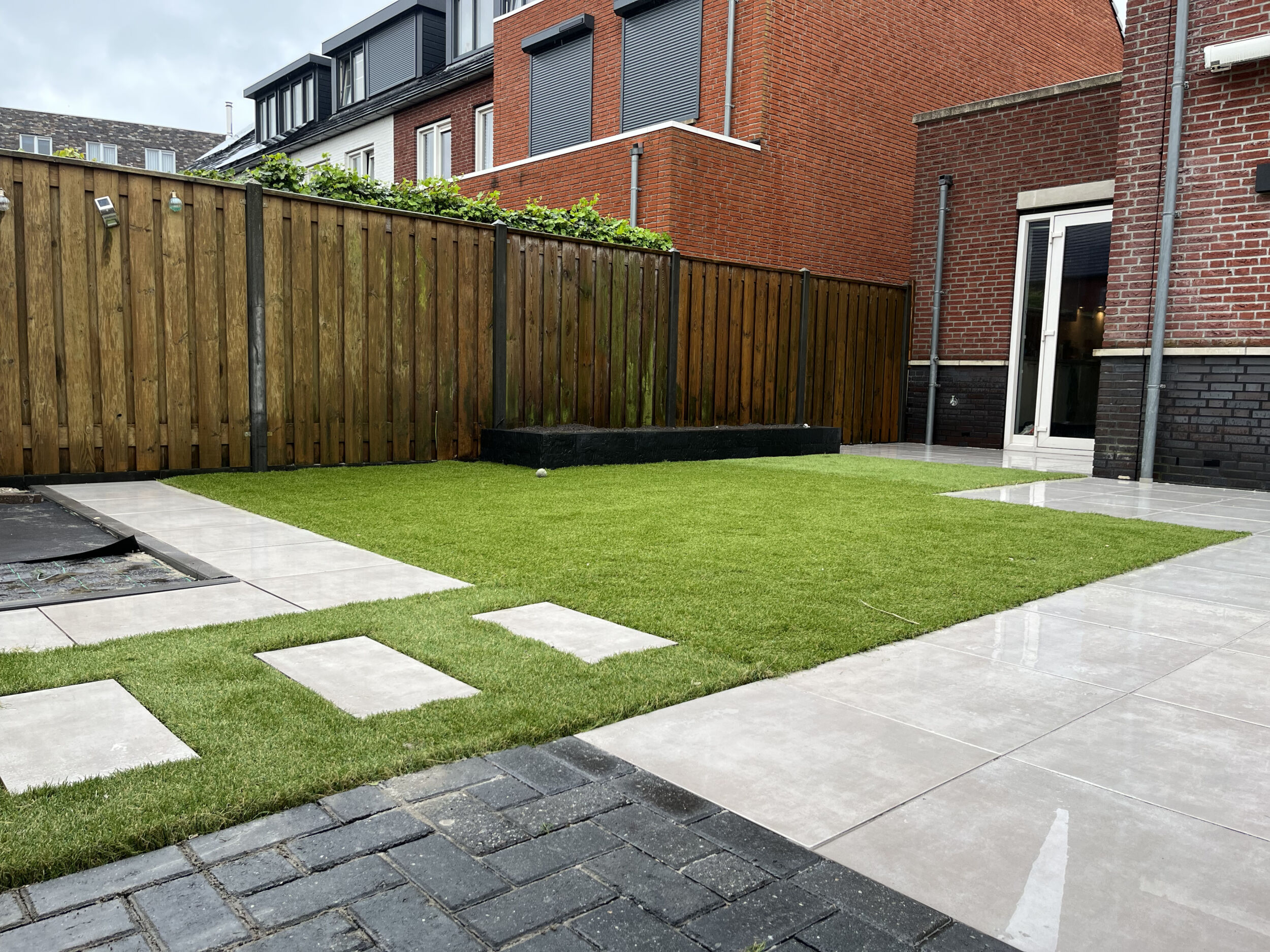 Een moderne en strak aangelegde tuin met gras, een net terras en een nieuwe schutting